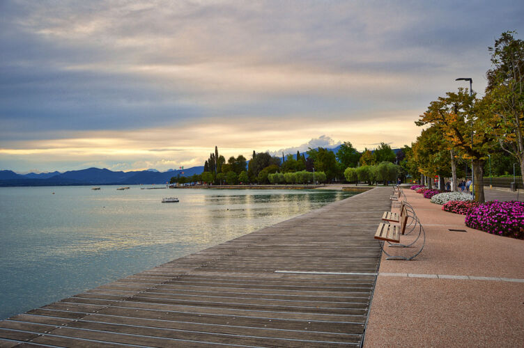 promenade pier of Bardolino, lake Garda with benches, flowers, trees, water and dramatic evening sky